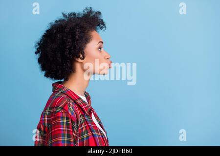 Profil Seite Foto von jungen afro Mädchen pouted Lippen senden Luftkuss suchen leeren Raum isoliert über blauen Hintergrund Stockfoto