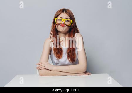 Kaukasische Frau sitzt am Tisch macht einen Schnurrbart mit Haaren Stockfoto