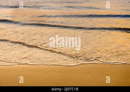 Nahaufnahme der ruhigen Meeresbrise, die bei Sonnenaufgang auf den Strand gespült wird Stockfoto