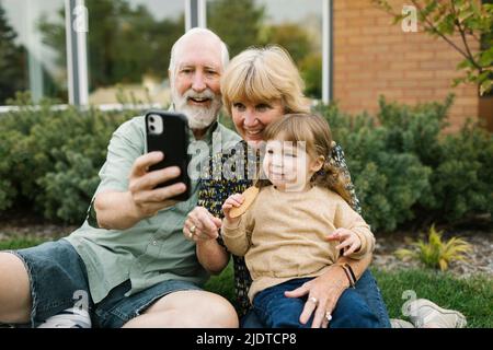 Lächelnde Großeltern machen Selfie mit Enkelin (4-5) im Garten Stockfoto