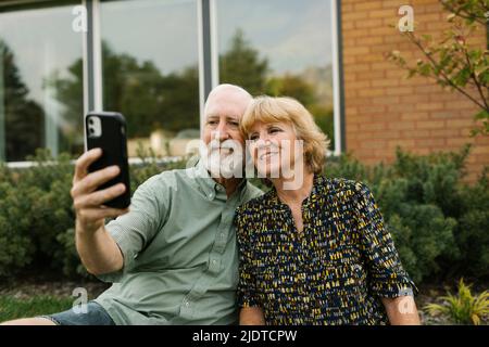 Lächelndes Seniorenpaar, das Selfie im Garten macht Stockfoto