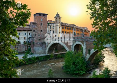 Malerisches abendliches Stadtbild des Tibers, der Fabrizio-Brücke und des Castello Caetani-Schlosses auf der Insel Isola Tiberina in Rom bei Sonnenuntergang. Stockfoto