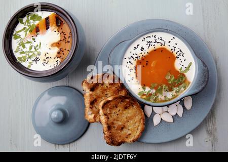 Kürbis-Herbstpüree-Suppe in einem Topf und einer Schüssel mit gegrillten Scheiben, Croutons und Milch auf einem blauen Holztisch. Draufsicht flach liegend Stockfoto