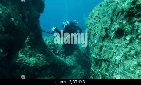 Taucher schwimmen durch einen Riss im Felsen. Riss im Meeresboden über tektonischen Platten. Die Tiktanische Verschiebung der Platten am Meeresgrund. Mediterr Stockfoto