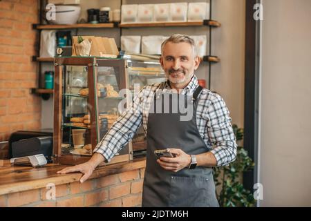 Mann hält Smartphone lächelnd auf die Kamera Stockfoto