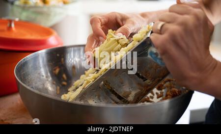 Nahaufnahme einer Frau, die mit einer Stahlreibe einen Apfel reibe, um eine Füllung für einen Kuchen oder ein Dessert vorzubereiten. Stockfoto