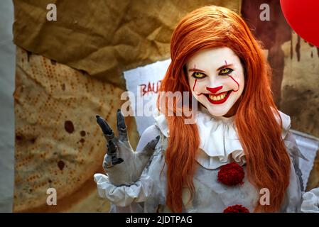 Pattensen, 4. Juni 2022: Junge hübsche Frau, die als böser Clown mit weiß gemaltem Gesicht gekleidet ist, streckt ihre Hand mit langen Fingernägeln vor Fantasie Stockfoto