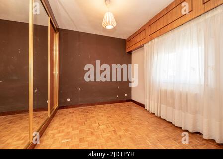 Leeres Schlafzimmer mit Einbauschrank mit Schiebetüren mit Spiegeln und Fenster mit weißen Vorhängen Stockfoto