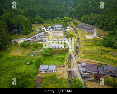 Luftaufnahme von Häusern und Schrein in kleiner Gemeinde durch Wald und Berge Stockfoto