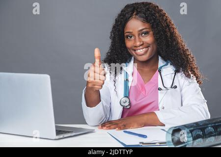 afroamerikanische lächelnde Ärztin, die am Tisch im medizinischen Büro sitzt und am Computer, Telemedizin, Online-Patientenberatung arbeitet Stockfoto