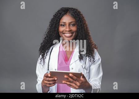 Glückliche professionelle Ärztin schwarze Frau im weißen Laborkittel mit Stethoskop und Tablet-pc Online-Konsultationen für ihre Patienten Stockfoto