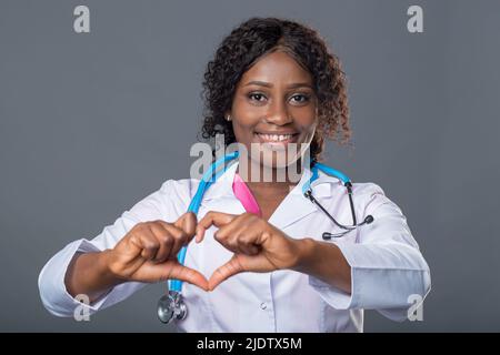 Eine afrikanische Ärztin in einem weißen Mantel und mit einem Stethoskop hält ein rotes Herz in ihren Händen. Kardiologin Stockfoto