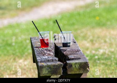 Zwei Plastikbecher, Becher oder Becher mit Trinkhalmen, die auf einer Bank in einem Park in England zurückgelassen wurden. Abfall, Vermüllung, Großbritannien Stockfoto