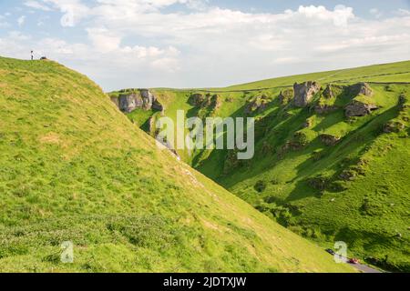 Derbyshire, Großbritannien – 5. April 2018: Zwei kleine Menschen stehen auf einem steilen Hügel mit Blick auf den Winnats Pass im Peak District National Park Stockfoto