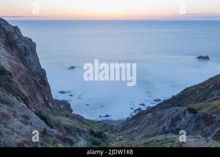 Verschwommene Wellen in der Dämmerung blauer Sonnenuntergang Langzeitaufnahme eines felsigen Abhangs, der zum Atlantischen Ozean im Sintra-Cascais Natural Park in Portuga führt Stockfoto