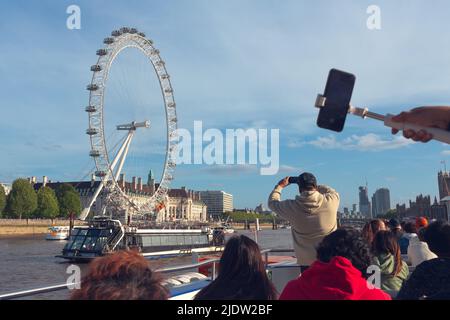 London, Großbritannien - 13. Mai 2022: Touristen fotografieren das London Eye von einem Boot auf der Themse aus. Stockfoto