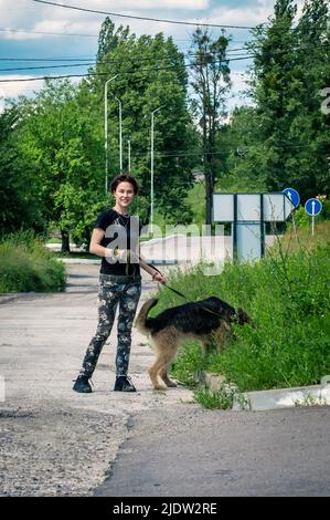 Fröhliche junge Frau, die ihren Hund an der Leine führt. Mädchen mit Spaß zu Fuß mit Hund. Freundschaft, Freizeit, Haustierkonzept. Stockfoto