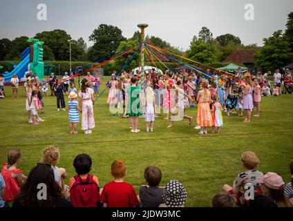 Kinder tanzen um einen Maibaum bei einem traditionellen Dorffest in England. Stockfoto