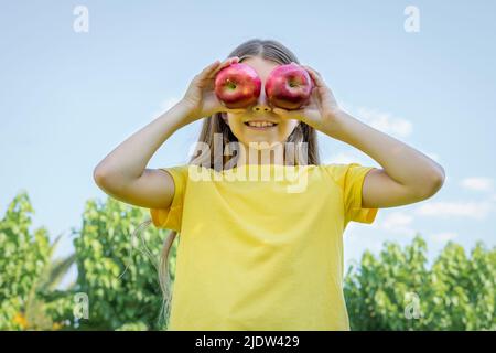 Ein Mädchen im Teenageralter hält im Park zwei Äpfel vor ihrem Gesicht. Stockfoto