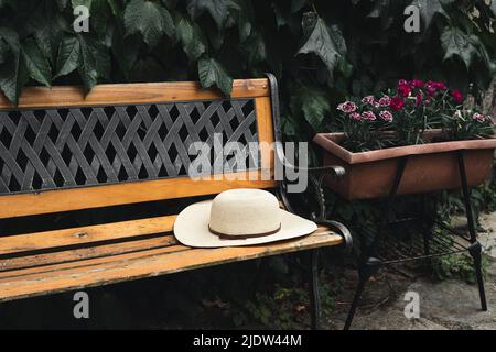 Eine Holzbank mit Damenhut im Garten, Cottagecore und Slow Life Konzept Stockfoto