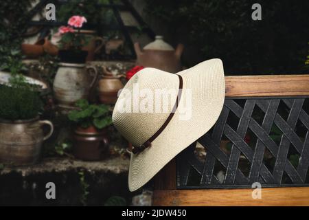 Frauen-Sommerhut auf einer Holzbank im Garten Nahaufnahme, pastorales und langsames Leben Konzept Stockfoto