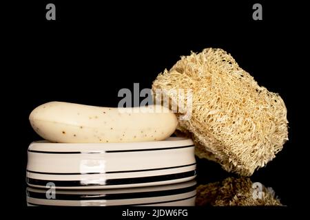 Ein Lufah-Duschschwamm und ein Stück Seife auf einer Seifenschale aus Keramik, Nahaufnahme isoliert auf schwarzem Hintergrund. Stockfoto