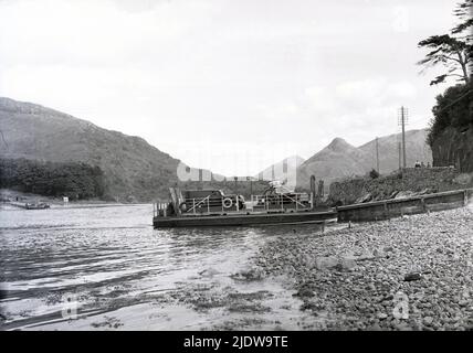 1950s, historisch, eine kleine Autofähre mit Plattform, die an einem Flussufer anlegt, schottische Highlands, Schottland, Großbritannien. Von den Hunderten von schottischen Offshore-Inseln sind 95 ganzjährig bewohnt und viele dieser abgelegenen Gemeinden können nur mit diesen kleinen Fähren erreicht werden. Stockfoto