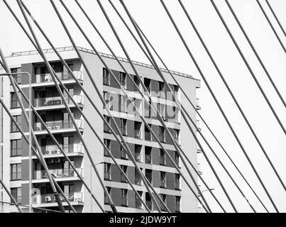 Schwarz-weiß minimalistisches abstraktes Bild mit einem Wohngebäude im Hintergrund und den Metallstangen oder Drähten einer Hängebrücke Stockfoto