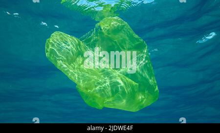 Plastikverschmutzung, Gelbe Plastiktüte schwimmt unter Wasser reflektiert auf der Oberfläche des blauen Wassers in Sonnenstrahlen. Weggeworfene Plastiktüten driften langsam Stockfoto