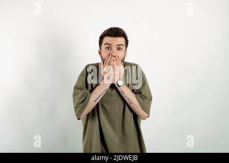 Porträt von beiläufigen jungen Mann trägt Freizeitkleidung posiert isoliert auf weißem Hintergrund schockiert decken Mund mit Händen aus Fehler, während. Geheim Stockfoto