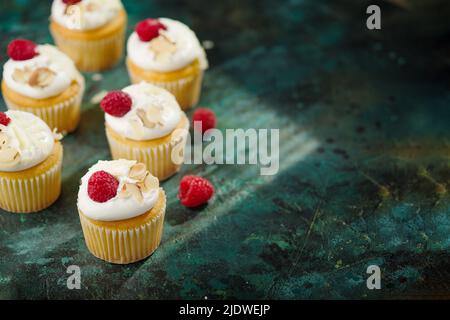 Süßes festliches Dessert: Leichte Cupcakes mit Creme und frischen Himbeeren auf grünem Marmorboden. Rezeptbuch, kulinarischer Blog, Restaurant und Zuhause Stockfoto