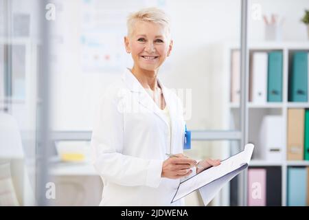 Porträt einer positiv selbstbewussten Ärztin im Laborkittel, die im Büro steht und mit medizinischen Akten arbeitet Stockfoto