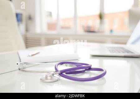 Konzentrieren Sie sich auf das moderne Stethoskop mit violettem Gummischlauch, das auf dem lichtdurchfluten Arzttisch im Büro aufgestellt wird Stockfoto
