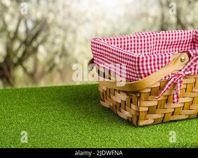 Auf dem üppigen grünen Gras, ein schöner Picknickkorb vor dem Hintergrund der Natur, blühende Bäume. Das Konzept der Sommer, Frühling Outdoor Erholung. Stockfoto