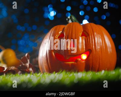 Lächelnder orangefarbener Kürbis auf grünem Gras vor einem fantasieblauen Himmel. Mystische Komposition für den Herbsturlaub - Halloween. Banner, Werbung, Invita Stockfoto