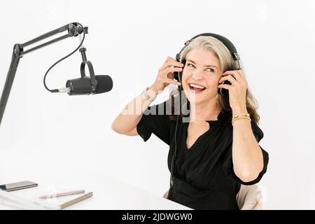 Frau mit Kopfhörern, die vor dem Mikrofon sitzt und lacht Stockfoto