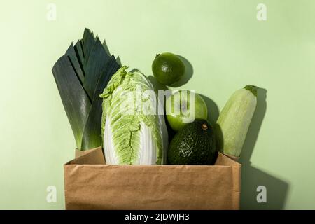 Monochromes Foto von frischem grünem Obst und Gemüse in einer Papiertüte auf grünem Hintergrund Stockfoto