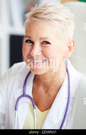 Portrait von glücklichen schönen reifen weiblichen Arzt mit blonden Haaren trägt Stethoskop um den Hals im Büro Stockfoto