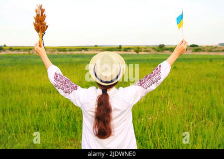 Unschärfe junge Frau in vyshywanka und Hut hält Bouquet von reifen goldenen Dornen von Weizen gebunden und Flagge auf der Wiese Natur Hintergrund. Flagge Ukrain Stockfoto