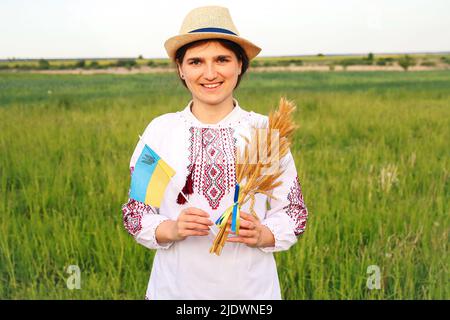 Unschärfe junge Frau in vyshywanka und Hut hält Bouquet von reifen goldenen Dornen von Weizen gebunden und Flagge auf der Wiese Natur Hintergrund. Flagge Ukrain Stockfoto