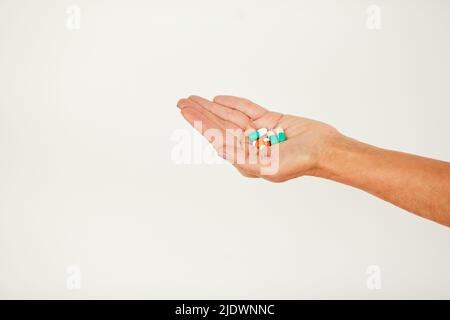 Nahaufnahme einer nicht erkennbaren Person, die eine Handvoll verschiedener Pillen und Antibiotika vor weißem Hintergrund hält Stockfoto
