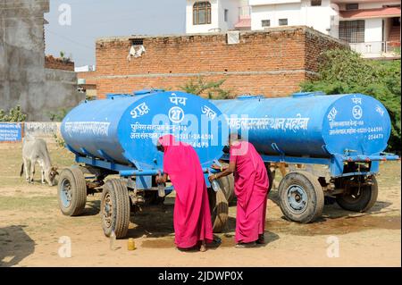 INDIEN, Uttar Pradesh, Bundelkhand, Mahoba, Wasserknappheit, Frauen in rosa Saree am blauen Wasserbehälter, der Plastikflasche mit Trinkwasser füllt, während einer Kundgebung der Frauenbewegung Gulabi Gang Stockfoto