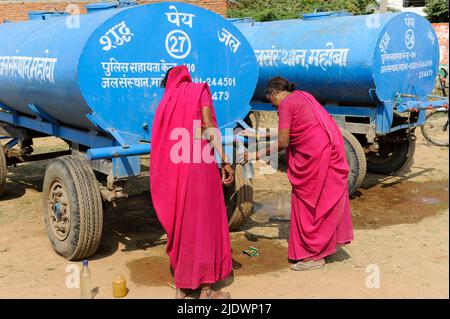 INDIEN, Uttar Pradesh, Bundelkhand, Mahoba, Wasserknappheit, Frauen in rosa Saree am blauen Wasserbehälter, der Plastikflasche mit Trinkwasser füllt, während einer Kundgebung der Frauenbewegung Gulabi Gang Stockfoto