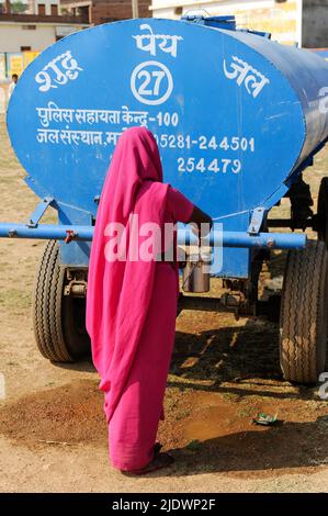 INDIEN, Uttar Pradesh, Bundelkhand, Mahoba, Wasserknappheit, Frauen in rosa Saree bei einer Kundgebung der Gulabi Gang beim Befüllen der Flasche mit Trinkwasser in einem blauen Wasserbehälter Stockfoto