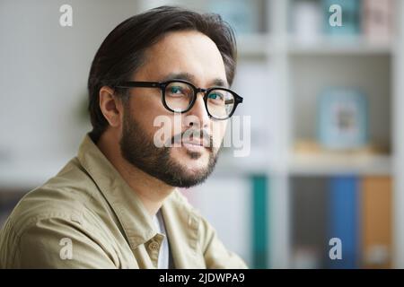 Porträt eines seriös selbstbewussten jungen asiatischen Mannes mit Bart und Schnurrbart in Brille und Hemd während der Arbeit im Büro Stockfoto