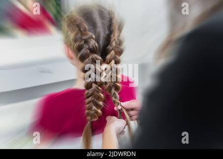 Friseur webt ein Zopf mit einem präjugendlich blonden Mädchen in einem Schönheits- und Friseursalon mit Bewegungsunschärfe-Effekt Stockfoto