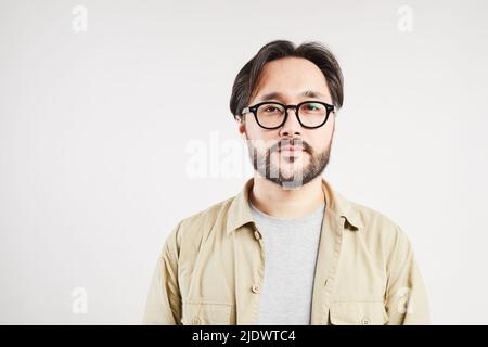 Porträt eines ernsthaften modernen jungen asiatischen Kerl in lässigem Hemd und Brille, die vor weißem Hintergrund steht Stockfoto