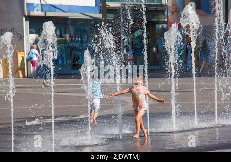 Wien, Österreich - 06.13.2022: Kinder tummeln sich in der Sommerhitze in den Jets des Stadtbrunnens Stockfoto