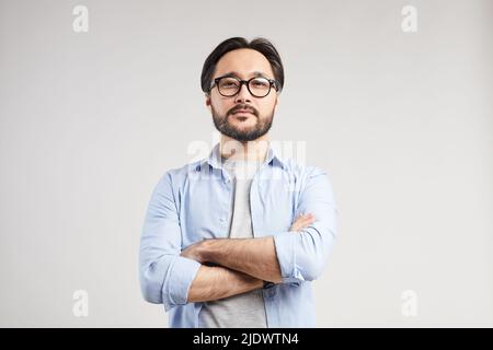 Serious selbstbewusst junge asiatische Web-Designer mit schwarzem Bart stehen vor isoliertem Hintergrund und Blick auf die Kamera Stockfoto