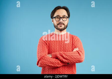 Asiatischer Mann mit Bart und Schnurrbart trägt einen stylischen Pullover vor blauem Hintergrund Stockfoto